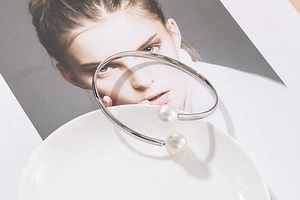 Detail of silver C-shaped open bracelet featuring two round white pearls on a white plate