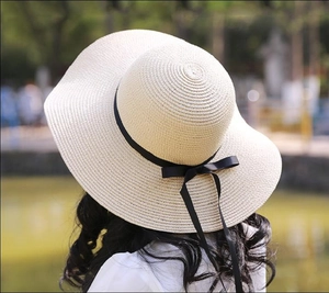 Detail of elegant straw beach hat with black ribbon bow and wide wavy brim