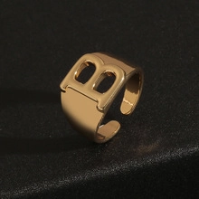 Close-up of golden letter B open ring with adjustable band on black texture