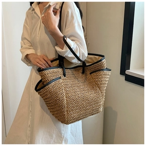 Detail of a large straw tote bag featuring black leather handles and beige woven texture