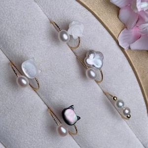 Eleganti anelli di perle con ciondoli a rosa e gatto in una scatola di velluto grigio