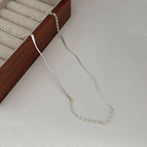 Macro shot of minimalist silver wavy bar pendant with delicate chain on wooden box