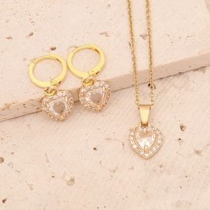 Close-up of gold heart necklace and earrings set with zircons on stone background