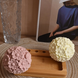 Detail of sphere flower shaped scented candles in pink and yellow on wooden tray
