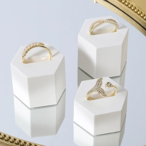 Golden fish tail and pearl rings on white hexagonal geometric jewelry display stands