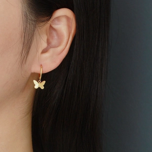 Pendientes de aro dorados con dije de mariposa mostrados en modelo con brillo fino