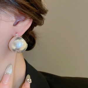 Detail view of large matte silver U-shaped basket earrings on a fashion model