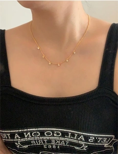 Detail of gold zircon necklace on model featuring sparkling round clear stone charms