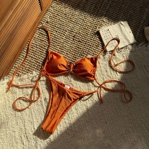 Rostorangefarbener Halter-Bikini mit Metallglanz und Ringdetail auf einer Matte