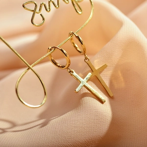 Polished gold cross earrings hanging on a display stand against pink silk fabric