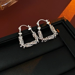 Macro detail of silver U-shaped earrings with pavé zircons on black leather surface