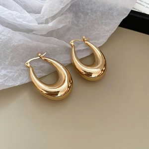 Detailed close-up of chunky gold C-shape hoop earrings on a minimalist beige background