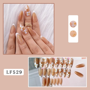 Detail view of French tip press-on nails with white flowers and gold foil accents