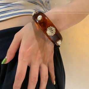 Detail of amber resin bangle with white imitation pearl and gold shell accents