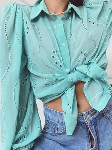 Detail of turquoise embroidered shirt featuring eyelet patterns and lace-up front closure