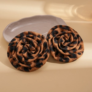 Close-up of leopard print fabric flower earrings on a textured ceramic tray