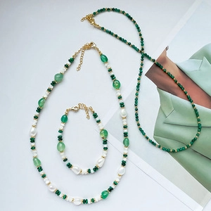 Detail of elegant gold jewelry set with green stones and pearls on a magazine background