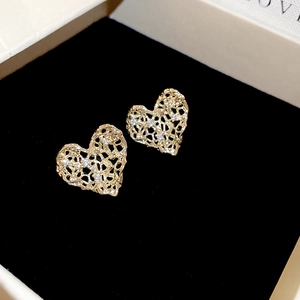 Detailed macro view of heart-shaped gold earrings with filigree mesh and white zircons