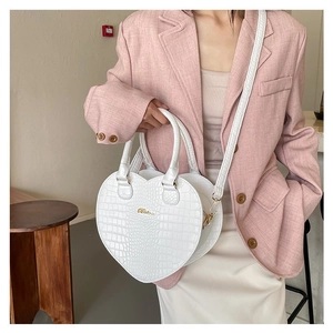Détail macro du sac à main cœur blanc motif crocodile avec logo doré et bandoulière