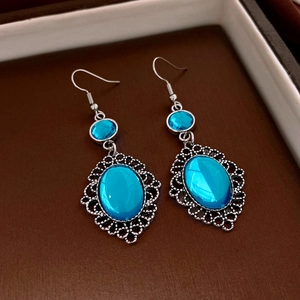 Dettaglio di orecchini vintage con resina blu ovale e motivi traforati in argento