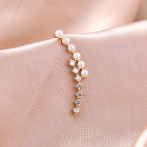 Elegant gold ear cuff with white pearls and sparkling zircons on pink silk background