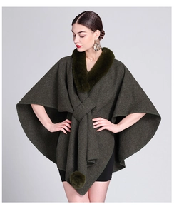 Detail of dark green knit poncho featuring a plush faux fur collar and pom-pom accents