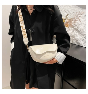 Detail of white half-moon saddle bag with wide patterned strap and gold lettering