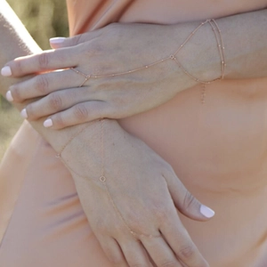 Detail of rose gold beaded hand chain bracelet with ring worn on a model's hand