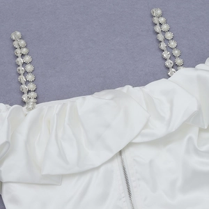 Detail of white satin dress featuring ruffled neckline and pearl rhinestone straps