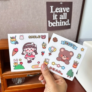 Close-up of cute cartoon person and animal themed stickers held against a warm desk background