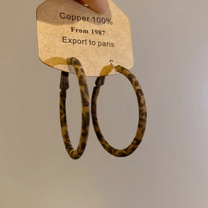 Détail de créoles en cuivre 100% avec pendentif cœur léopard tenues à la main
