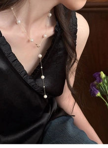 Detailed view of French vintage pearl Y-necklace on black silk dress with golden chain