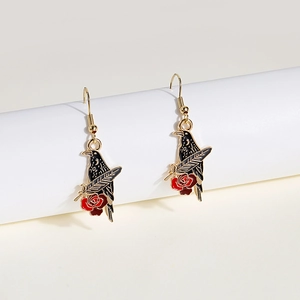 Detail of gothic raven earrings with red rose and feather charms on white stand