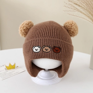 Vue détaillée du bonnet en tricot marron pour bébé avec broderies d'ours et pompons