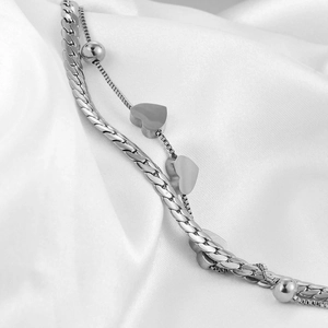 Detail of silver double-layered bracelet with curb chain and heart charm on white satin