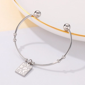 Macro detail of silver stainless steel open bangle with engraved square charm and icons