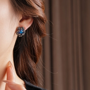 Nahaufnahme eines sternförmigen Ohrrings mit blauem Edelstein am Ohr des Models getragen