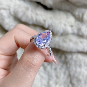 Close-up of a pear-shaped purple gemstone ring with diamond halo worn on finger