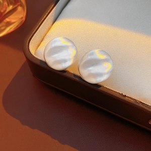 Macro shot of silver textured round earrings on a satin pad with elegant warm lighting