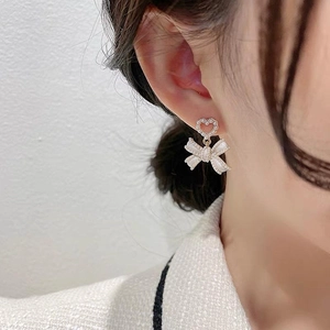 Elegant pearl bow earrings with heart studs worn by a model for a stylish look