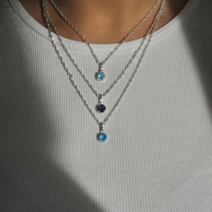 Close-up of layered silver birthstone necklaces featuring blue and purple round pendants