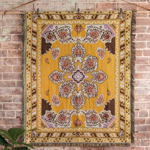 Close-up of Bohemian yellow mandala woven blanket with fringe on a rustic brick wall