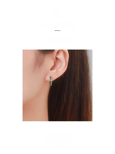 Detail view of gold hoop earrings with green enamel coating and colored cubic zirconia