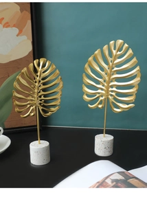 Modern gold monstera leaf metal sculpture with white terrazzo base for home decor