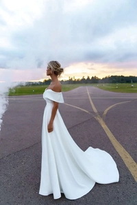 Dramatic long shot of white off-the-shoulder satin wedding dress with elegant sweeping train