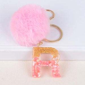 Macro shot of resin letter R keychain with pink pompom and gold foil flakes detail