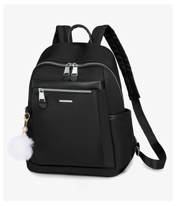 Detail of black nylon backpack featuring silver zippers and a white faux fur ball pendant