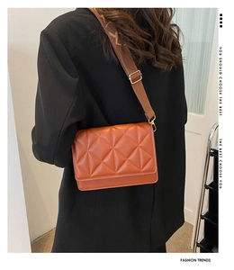 Detail of a brown quilted leather crossbody bag with an embroidered wide canvas strap