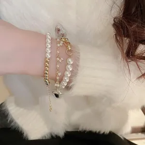 Three-piece gold chain and white pearl bracelet set with heart pendant on a model