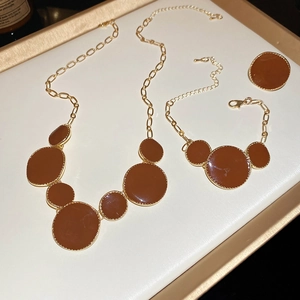 Parure de bijoux vintage dorée avec pendentifs ronds marrons sur un plateau blanc